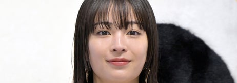 セレブが黒いボタンの付いた白いドレスを着て、ルイ・ヴィトンのバッグを持ちながらイベントでポーズを取っている。