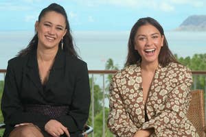 Two people are sitting and smiling outdoors; one wears a dark blazer, the other a patterned outfit