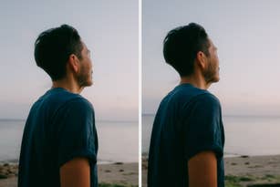 A person with short dark hair stands on a beach, looking at the horizon. They wear a casual short-sleeved shirt, enjoying a peaceful moment